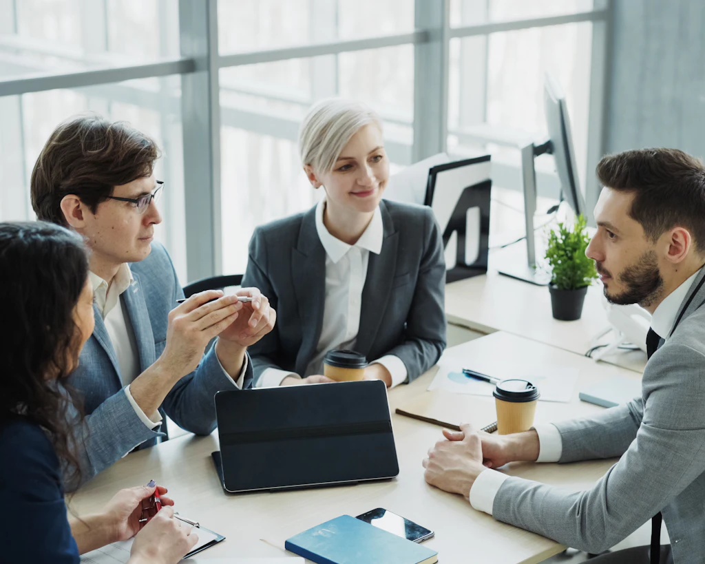 Vier Fachpersonen besprechen Unterlagen an einem Besprechungstisch in einem hellen Büro