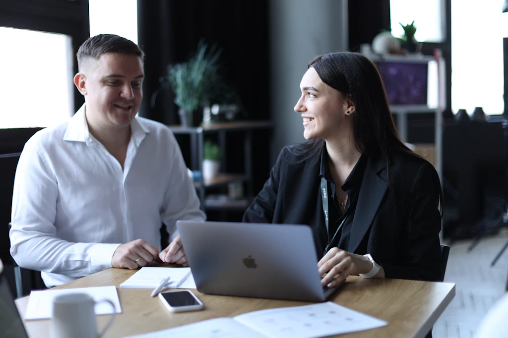 Zwei Personen im Gespräch an einem Tisch mit Laptop und Notizen
